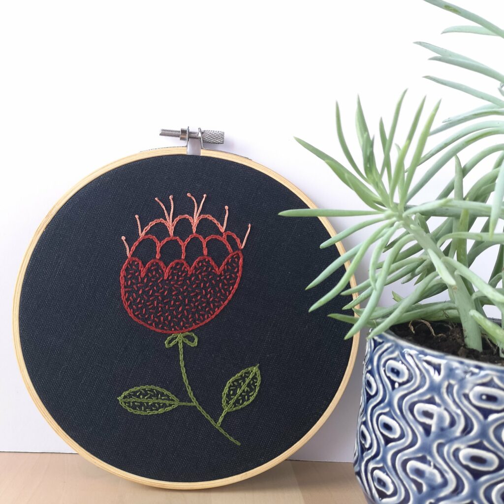 Red abstract flower hand embroidered hoop on navy blue fabric near a succulent plant
