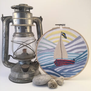 Sailboat hand embroidery in a hoop with lamp and stones